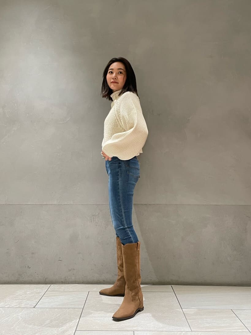ベージュ系のブーツ、ホワイト系のニット/セーター、ブルー系のデニムパンツを着用したレディースの秋コーディネートの2枚目の写真