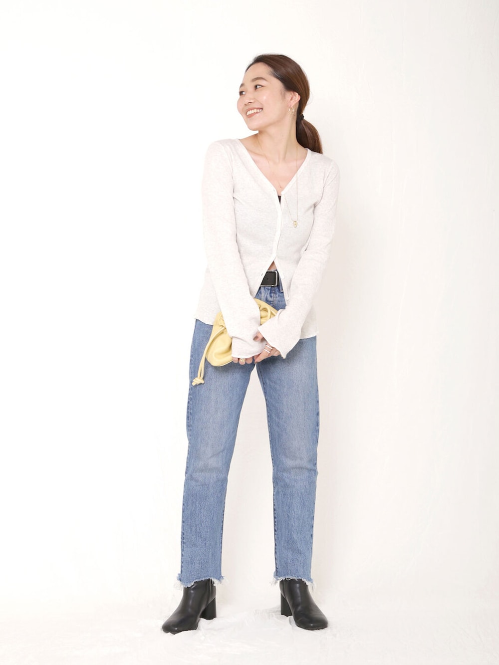 イエロー系のクラッチバッグ、ブルー系のデニムパンツ、ブラック系のブーツを着用したレディースの秋コーディネートの2枚目の写真