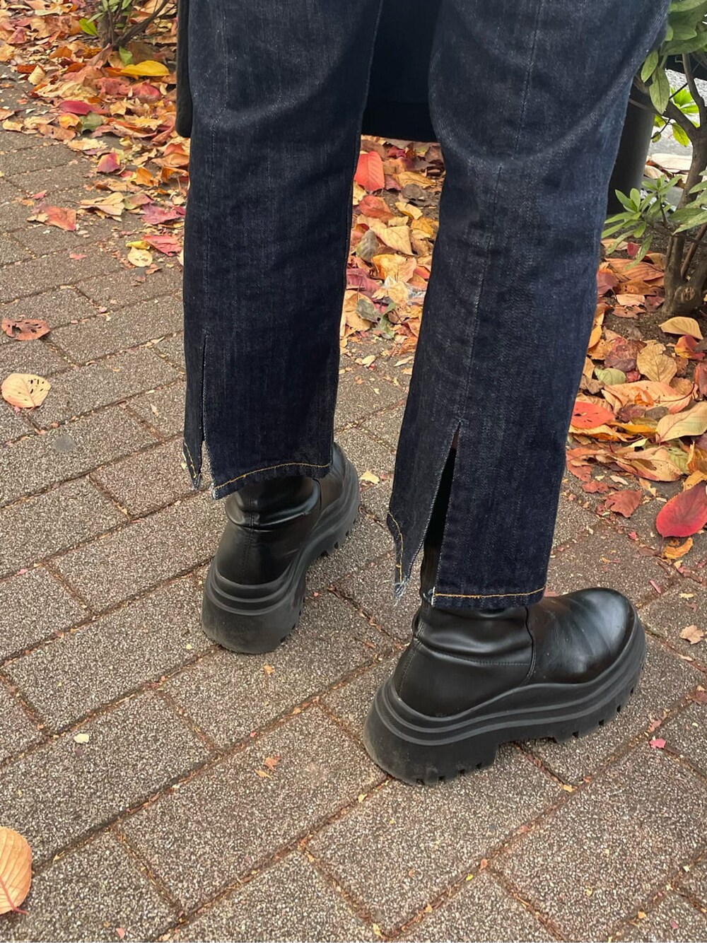 ブルー系のデニムパンツ、ブラック系のチェスターコート、レッド系のニット/セーターを着用したレディースの秋コーディネートの4枚目の写真