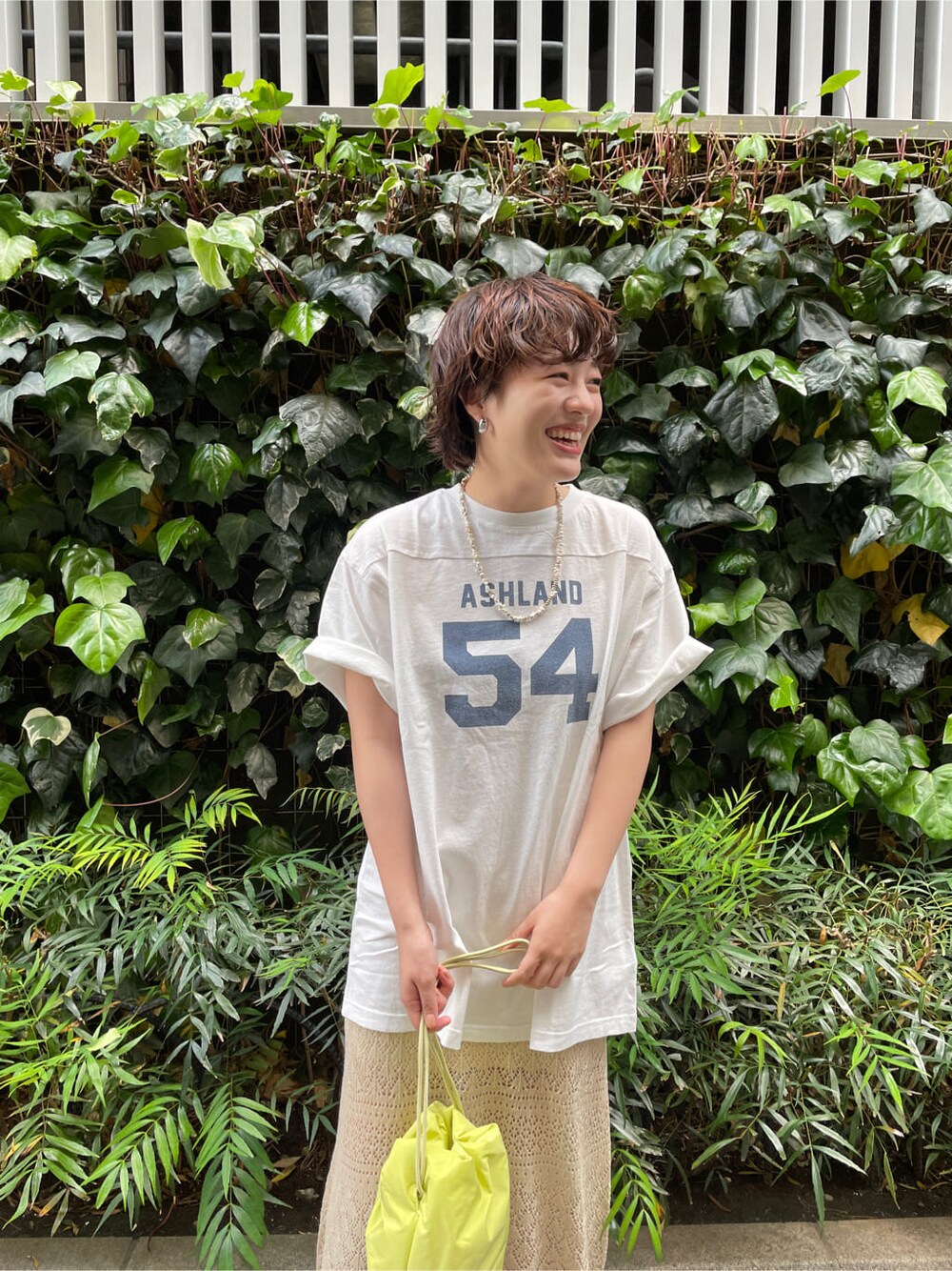 グリーン系のハンドバッグ、ホワイト系のTシャツ/カットソー、ベージュ系のスカートを着用したレディースの春コーディネートの6枚目の写真