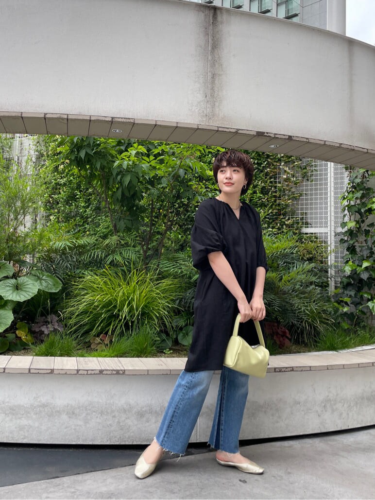 グリーン系のハンドバッグ、ブラック系のワンピース、ブルー系のデニムパンツを着用したレディースの春コーディネートの2枚目の写真