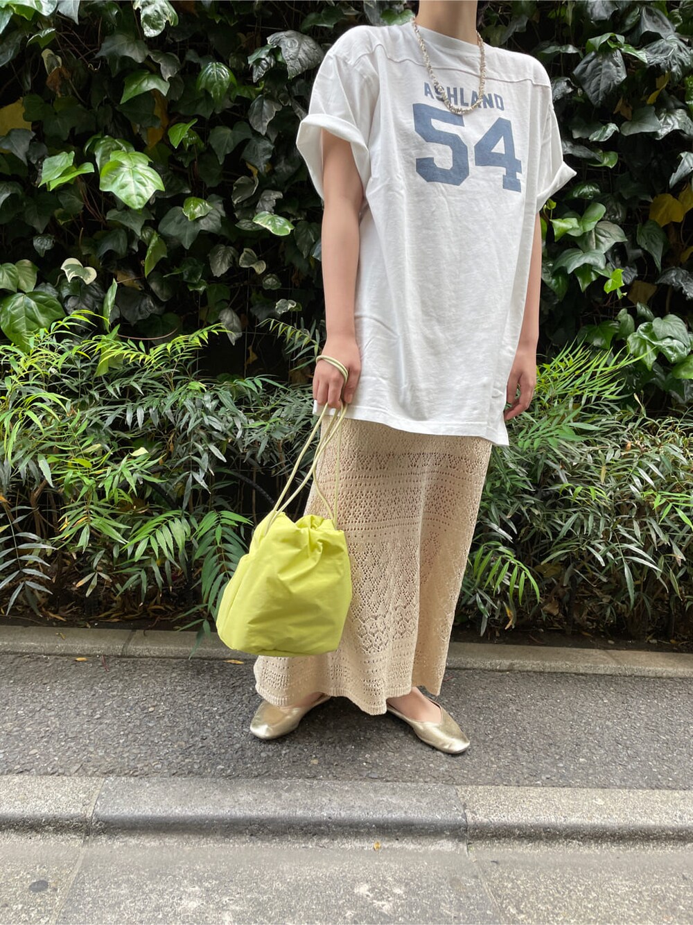 グリーン系のハンドバッグ、ホワイト系のTシャツ/カットソー、ベージュ系のスカートを着用したレディースの春コーディネートの2枚目の写真