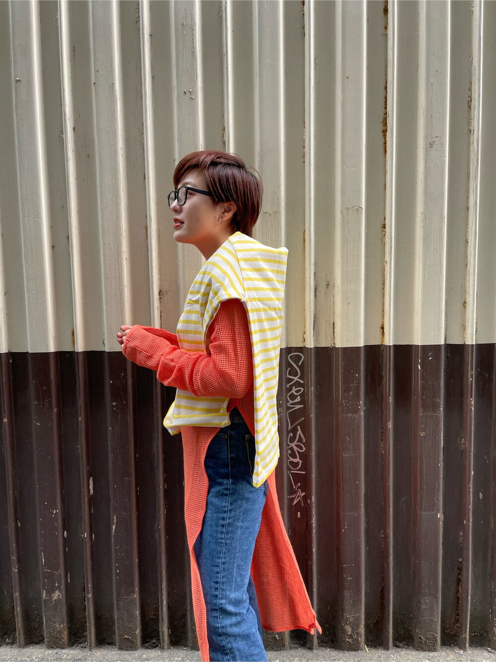 ブルー系のデニムパンツ、オレンジ系のワンピースを着用したレディースの春コーディネートの3枚目の写真