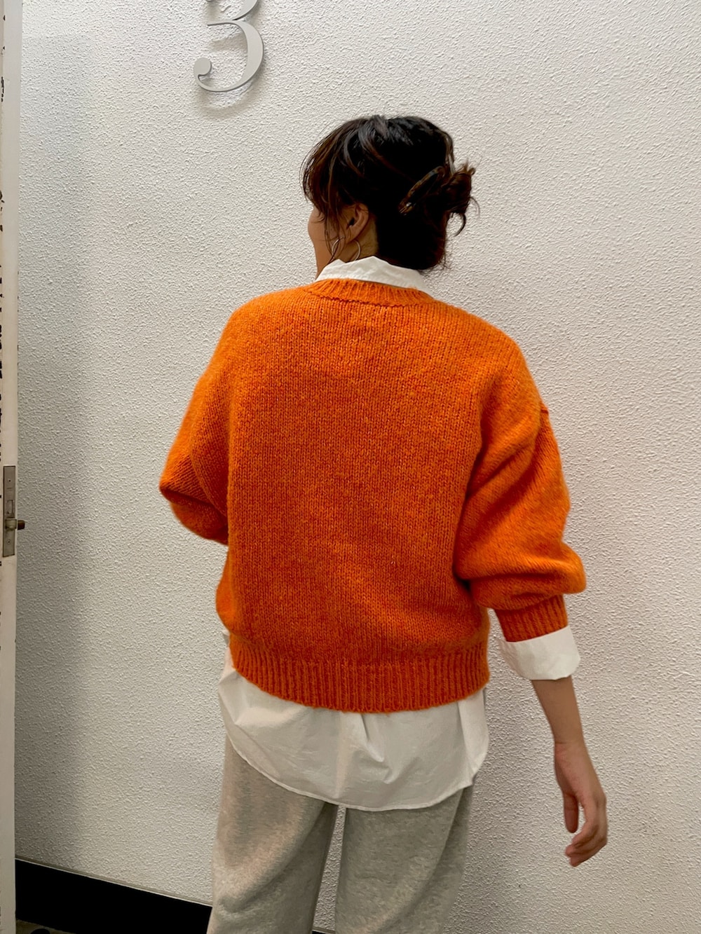 オレンジ系のニット/セーター、ホワイト系のシャツ/ブラウス、グレー系のスウェットパンツを着用したレディースの秋コーディネートの2枚目の写真