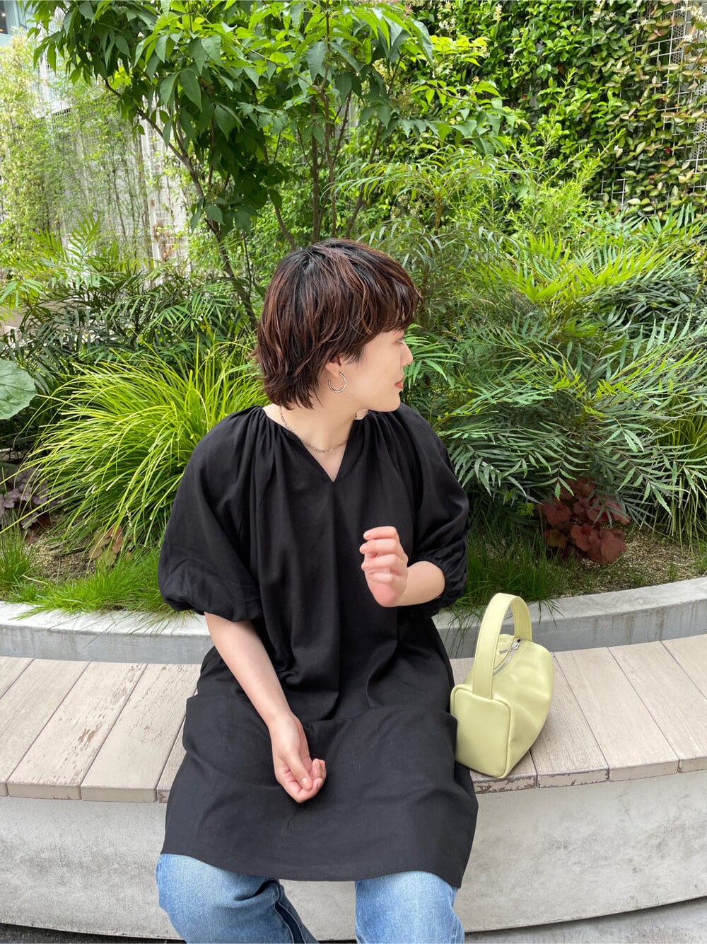 グリーン系のハンドバッグ、ブラック系のワンピース、ブルー系のデニムパンツを着用したレディースの春コーディネートの5枚目の写真