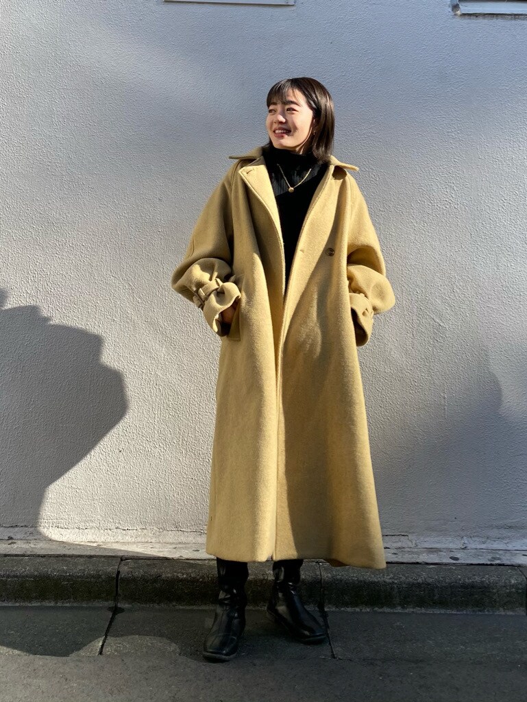 イエロー系のステンカラーコートを着用したレディースの冬コーディネートの3枚目の写真