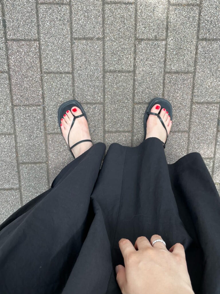 ブラック系のワンピース、ブラック系のサンダル、オレンジ系のストール/ショールを着用したレディースの夏コーディネートの6枚目の写真