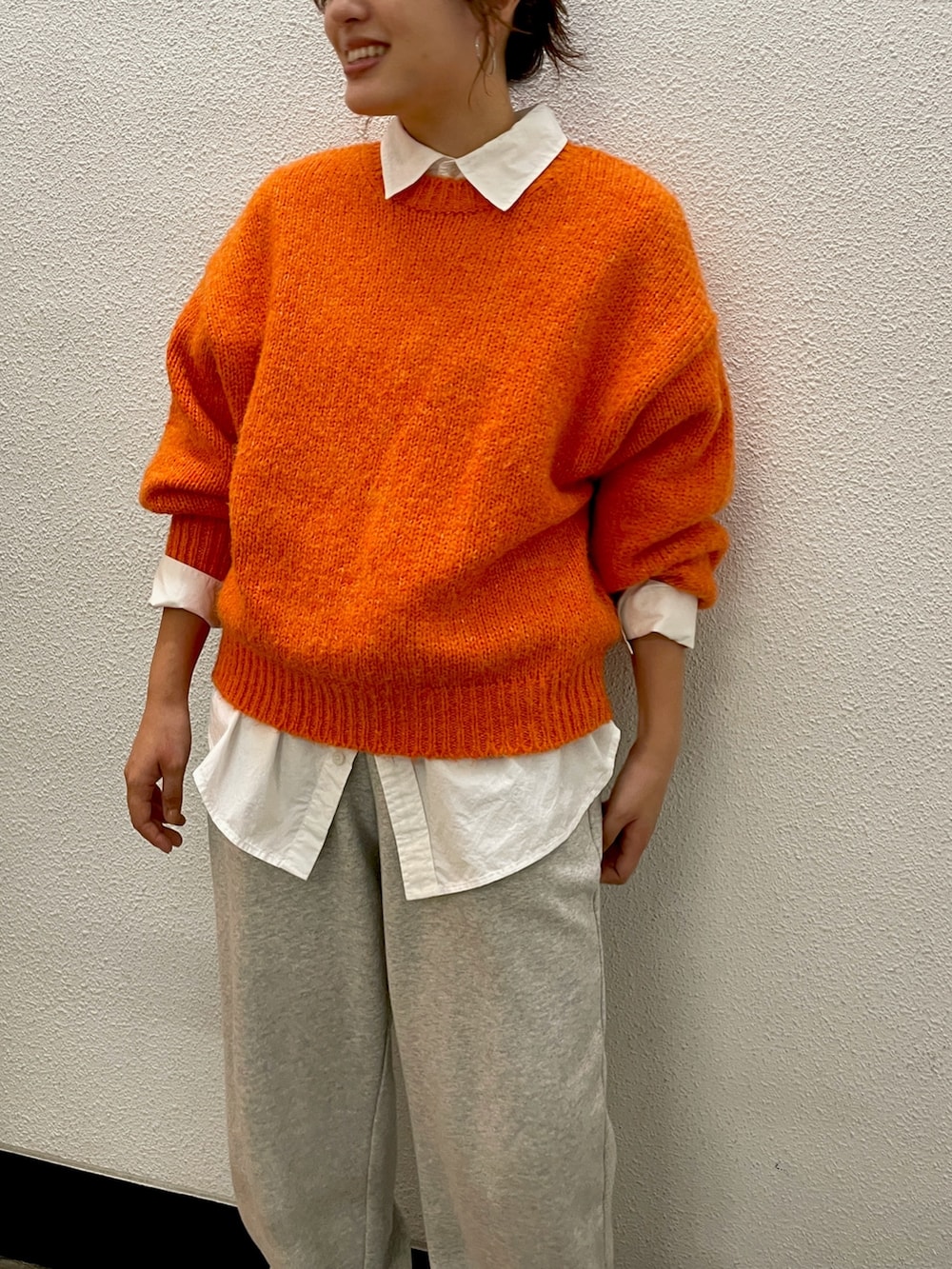 オレンジ系のニット/セーター、ホワイト系のシャツ/ブラウス、グレー系のスウェットパンツを着用したレディースの秋コーディネートの3枚目の写真