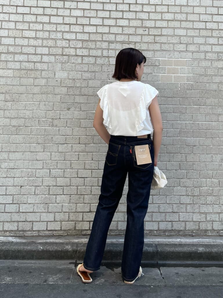 ブルー系のデニムパンツ、ホワイト系のクラッチバッグ、ホワイト系のTシャツ/カットソーを着用したレディースの夏コーディネートの3枚目の写真