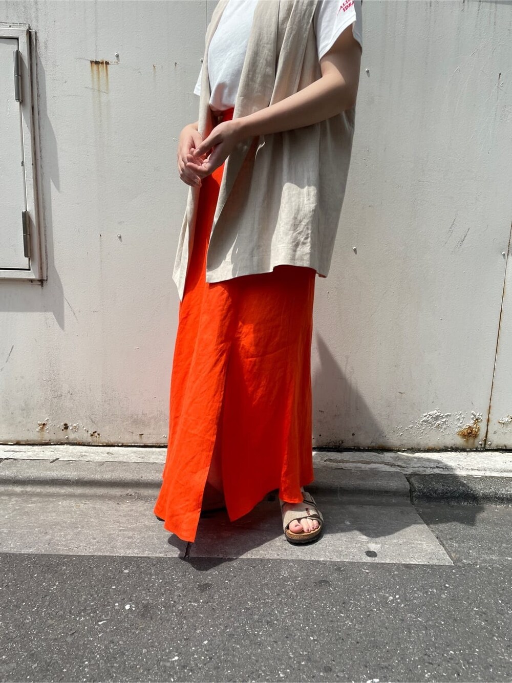 ホワイト系のベスト、ホワイト系のTシャツ/カットソー、オレンジ系のスカートを着用したレディースの夏コーディネートの2枚目の写真