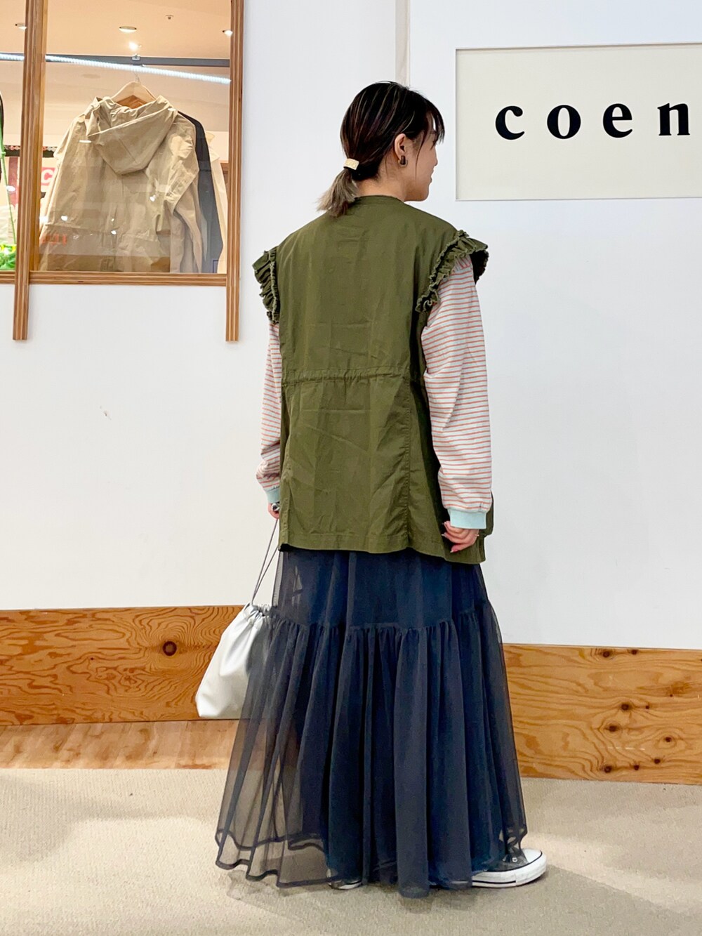 グリーン系のベスト、オレンジ系のTシャツ/カットソー、グレー系のスカートを着用したレディースの春コーディネートの4枚目の写真