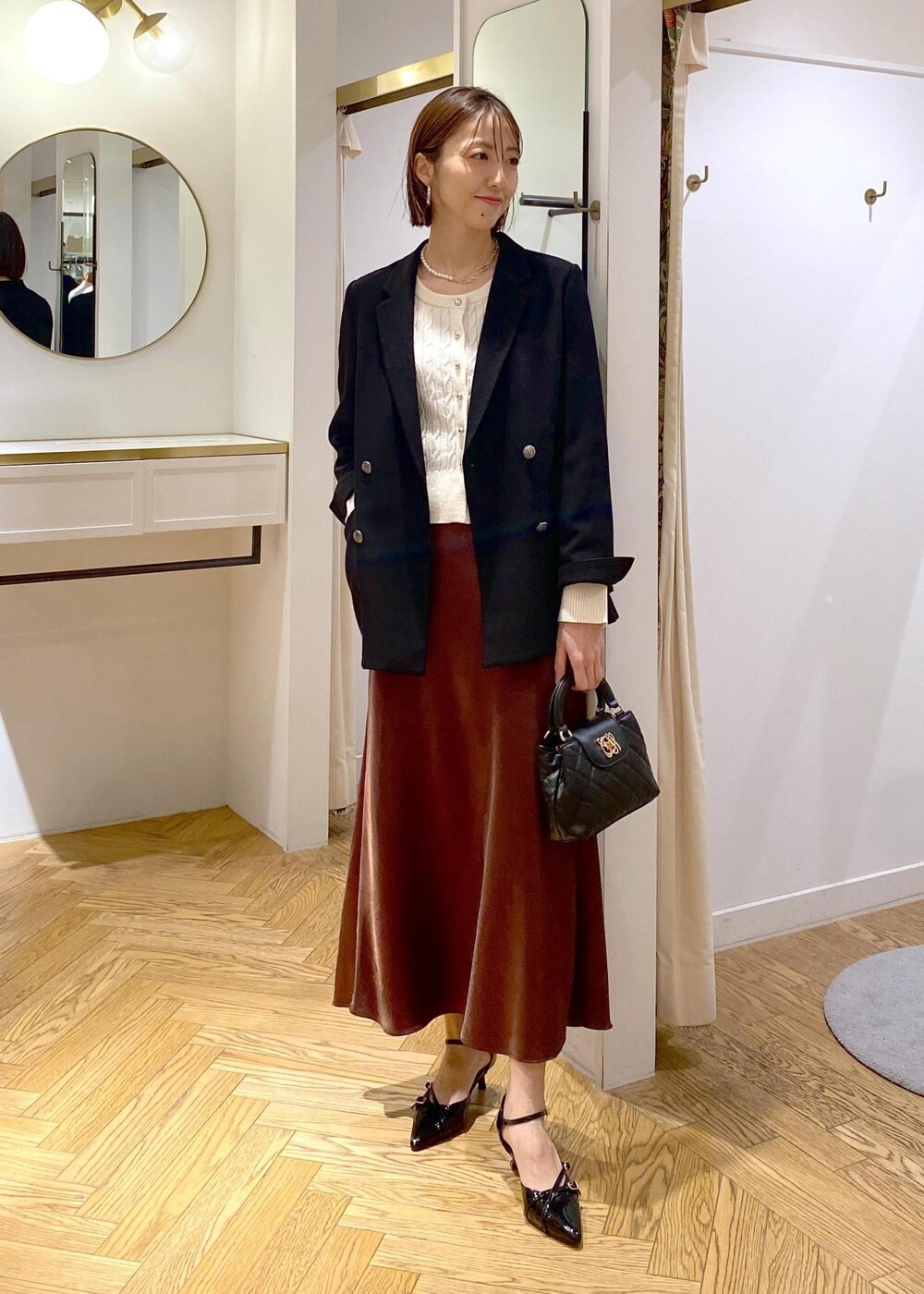 ブラック系のテーラードジャケット、ブラック系のパンプス、ブラウン系のスカートを着用したレディースの冬コーディネートの10枚目の写真