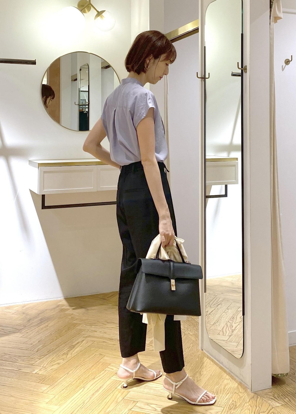 ブラック系のハンドバッグ、ホワイト系のカーディガン/ボレロ、ブラック系のスラックスを着用したレディースの夏コーディネートの2枚目の写真