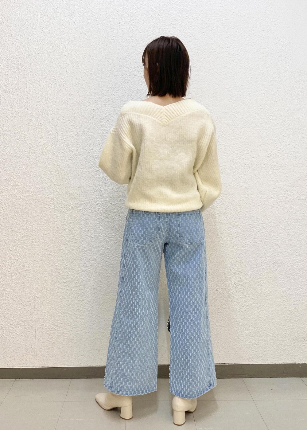 シルバー系のハンドバッグ、ホワイト系のニット/セーター、ブルー系のデニムパンツを着用したレディースの冬コーディネートの2枚目の写真