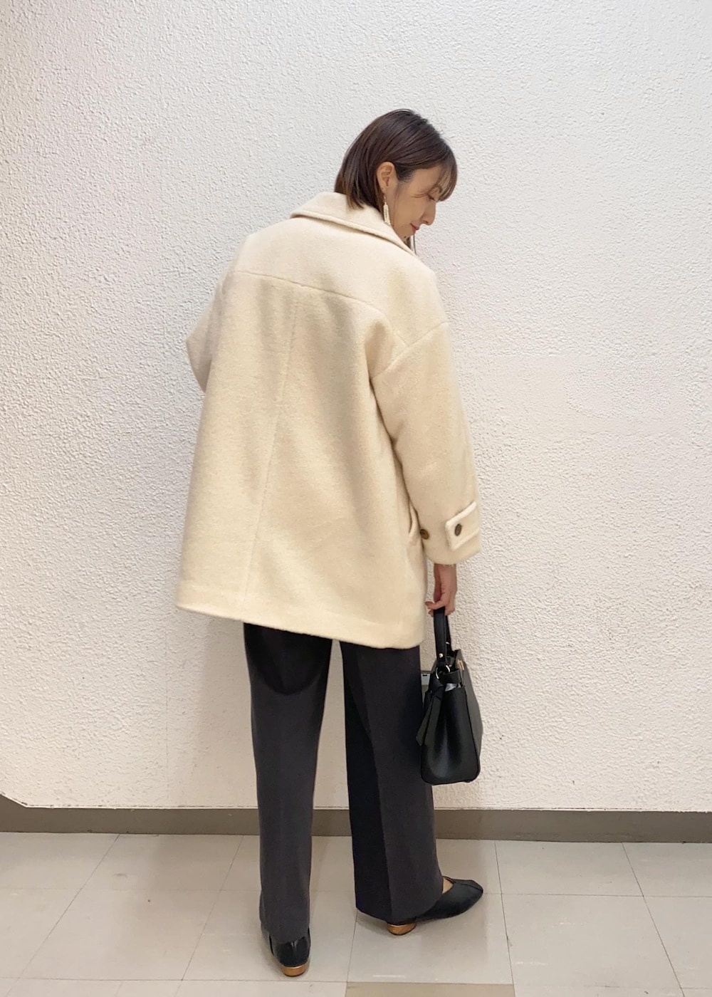 ブラック系のハンドバッグ、ホワイト系のピーコート、ピンク系のニット/セーターを着用したレディースの冬コーディネートの2枚目の写真