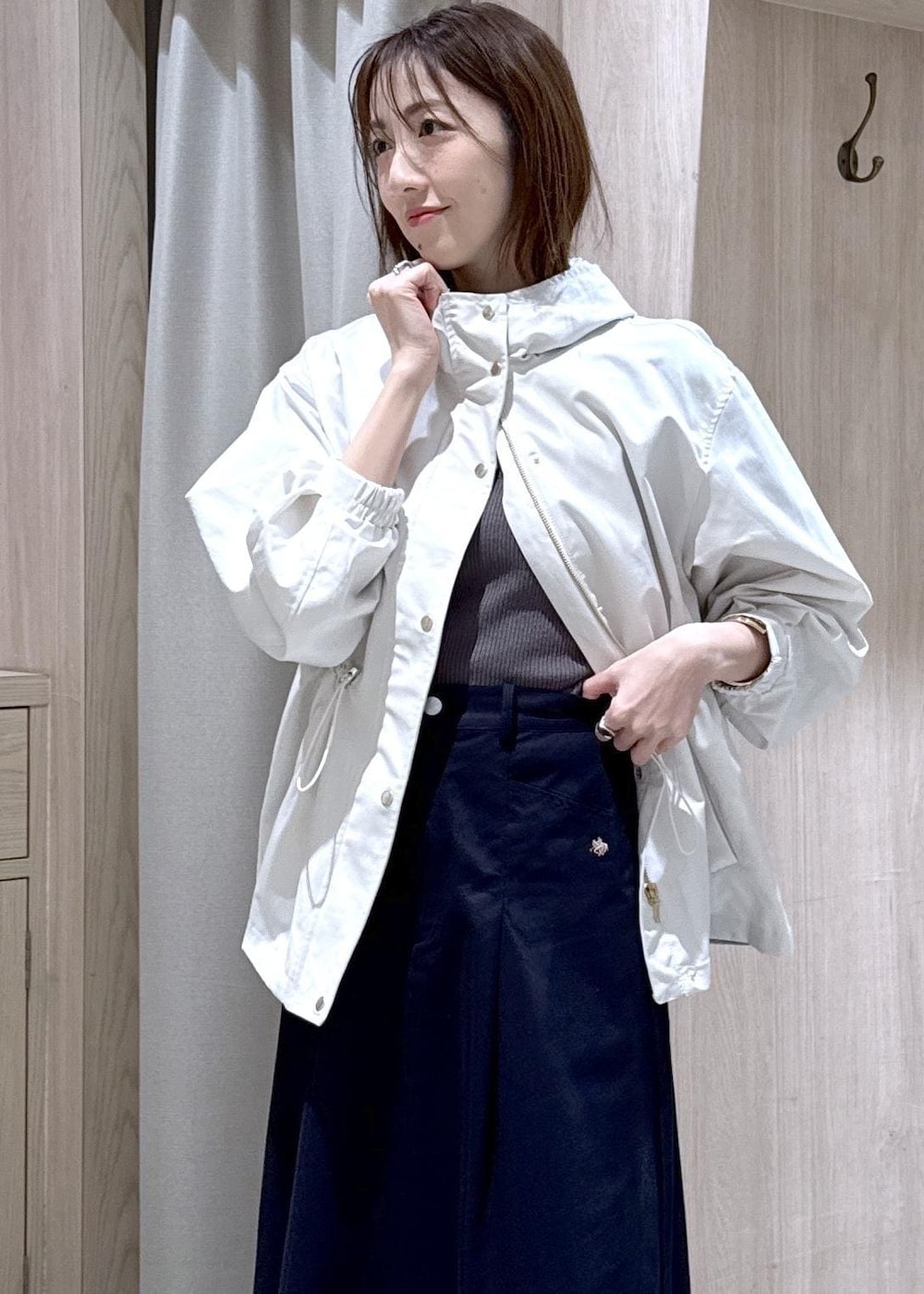 グレー系のニット/セーター、ブルー系のスカート、ホワイト系のナイロンジャケットを着用したレディースの春コーディネートの4枚目の写真