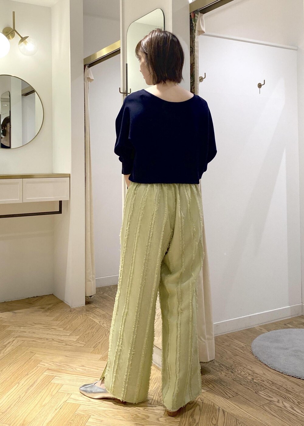 シルバー系のパンプス、グリーン系のスラックス、ブラック系のショルダーバッグを着用したレディースの春コーディネートの2枚目の写真