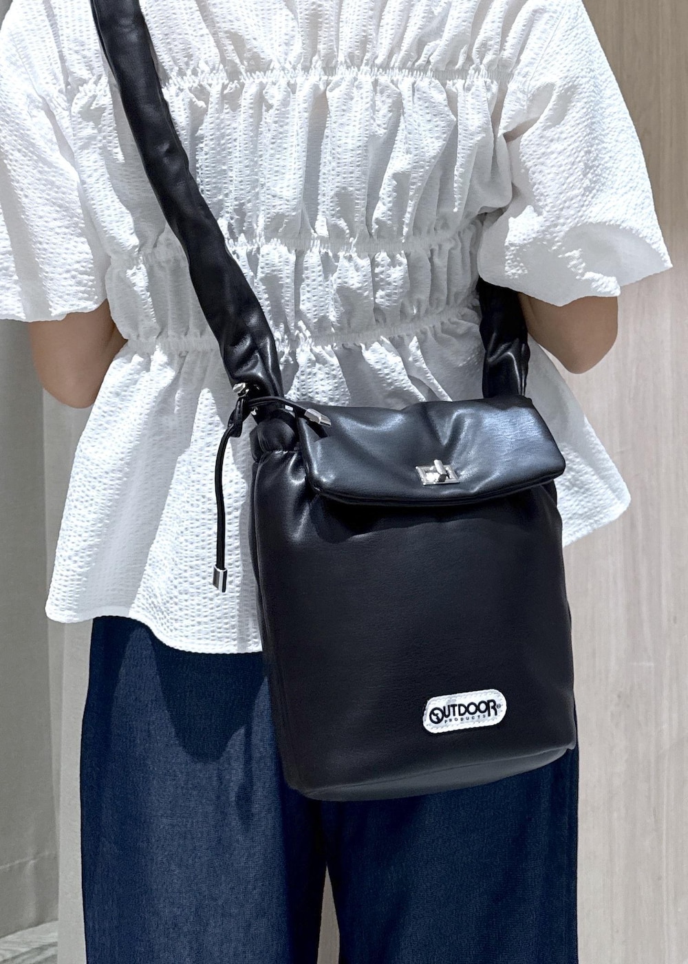 ブラック系のショルダーバッグ、ブラック系のパンプス、ブルー系のデニムパンツを着用したレディースの夏コーディネートの7枚目の写真
