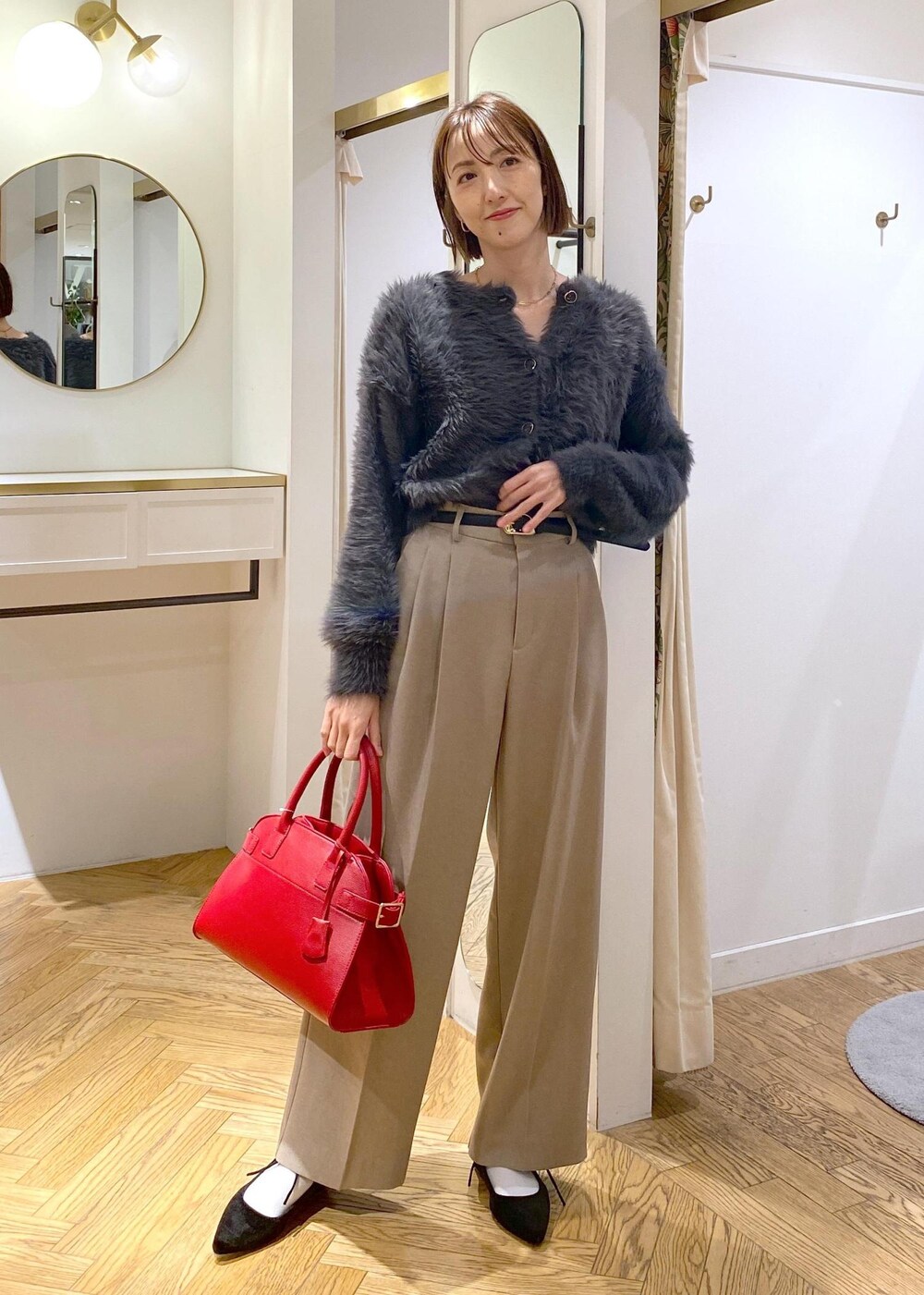 レッド系のトートバッグ、ベージュ系のスラックス、グレー系のカーディガン/ボレロを着用したレディースの冬コーディネートの2枚目の写真