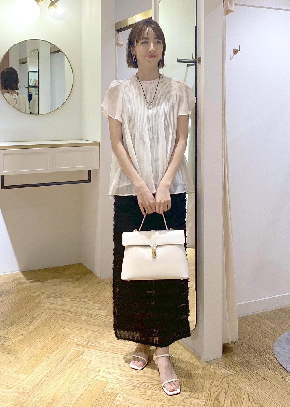 ホワイト系のハンドバッグ、ホワイト系のサンダル、ブラック系のスカートを着用したレディースの春コーディネートの4枚目の写真