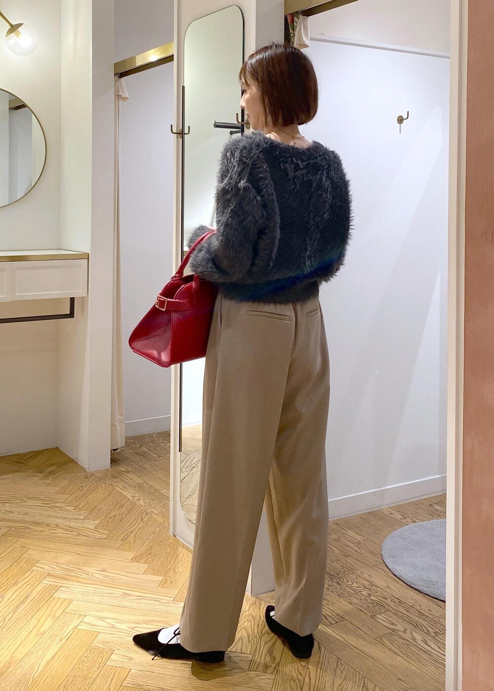 レッド系のトートバッグ、ベージュ系のスラックス、グレー系のカーディガン/ボレロを着用したレディースの冬コーディネートの3枚目の写真