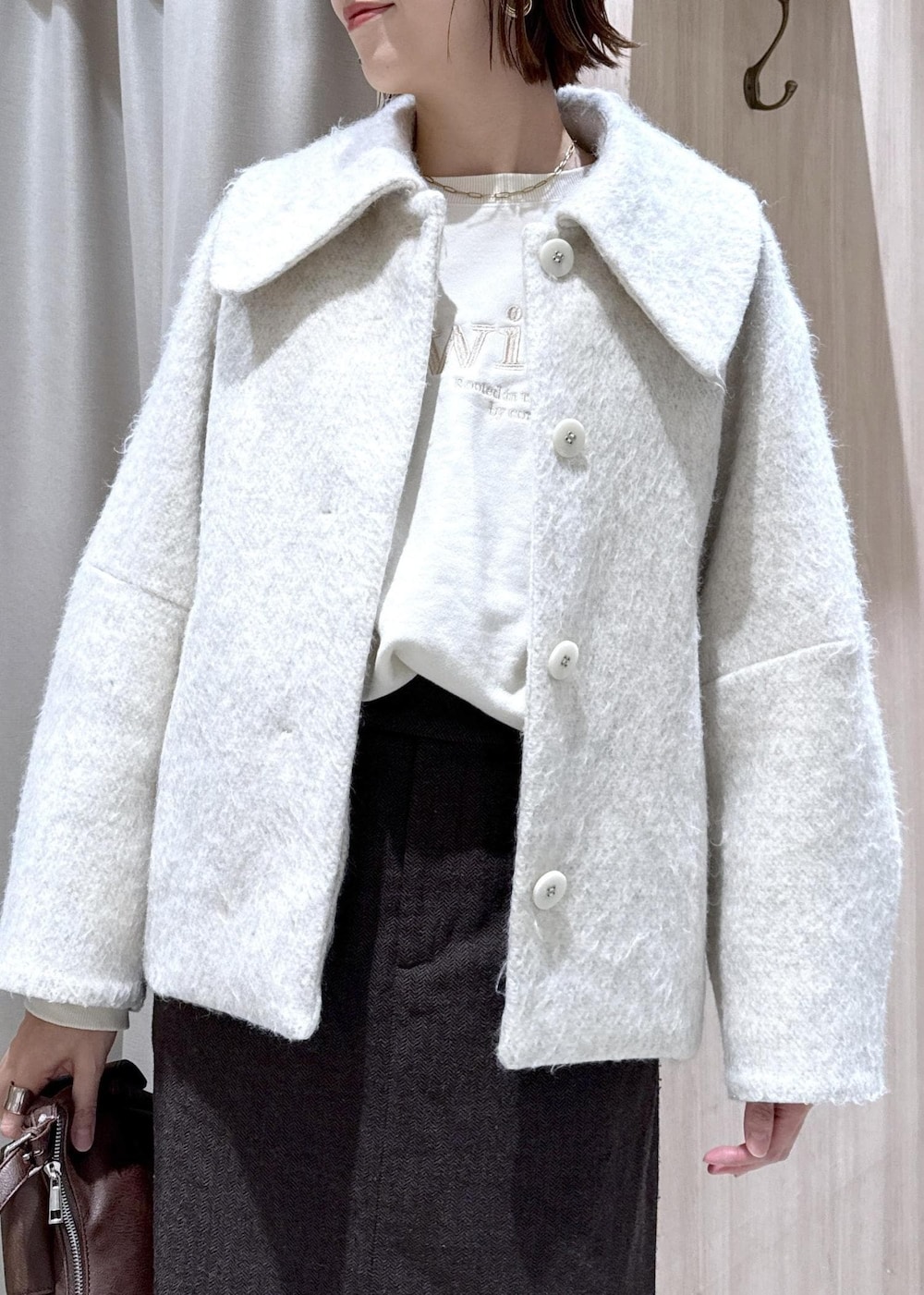 ブラウン系のショルダーバッグ、ブラック系のブーツ、ホワイト系のブルゾンを着用したレディースの秋コーディネートの6枚目の写真