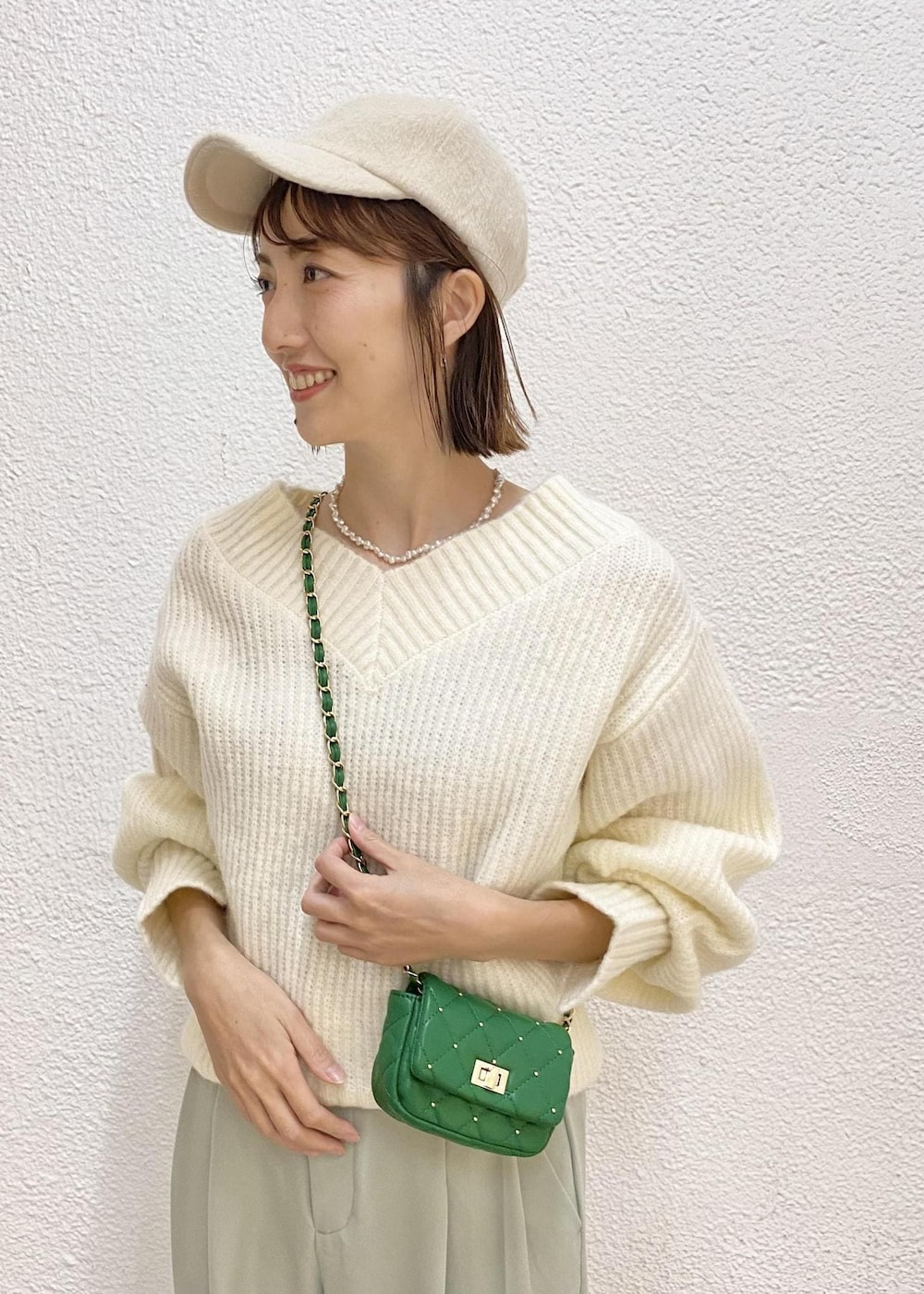 グリーン系のスラックス、グリーン系のショルダーバッグ、ホワイト系のニット/セーターを着用したレディースの冬コーディネートの3枚目の写真