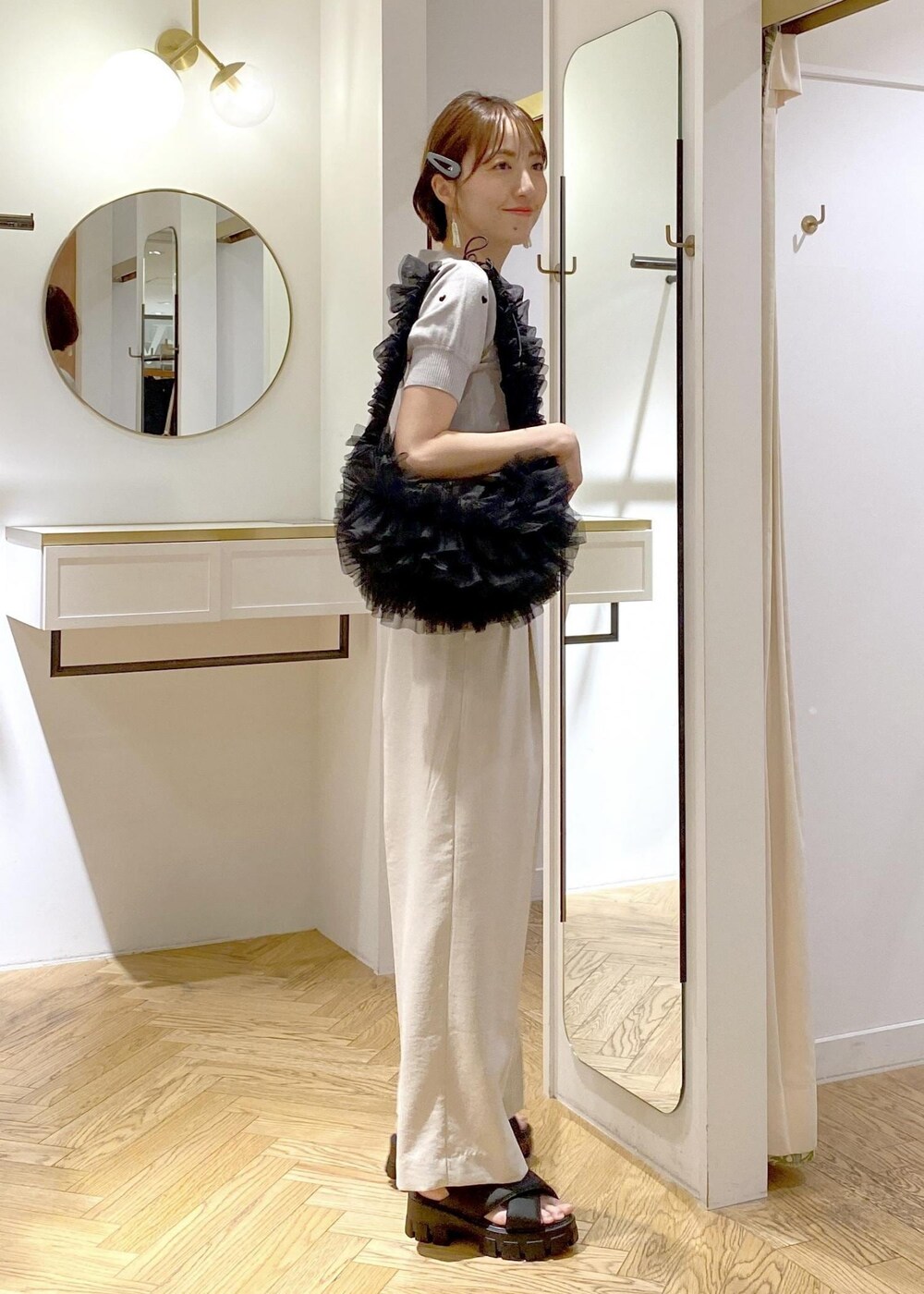 ブラック系のショルダーバッグ、グレー系のニット/セーター、ホワイト系のスラックスを着用したレディースの夏コーディネートの3枚目の写真