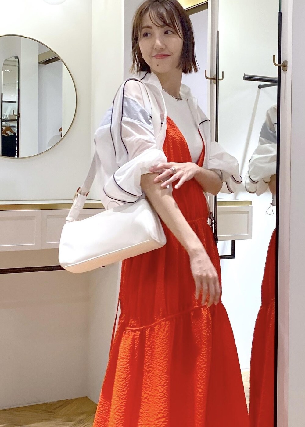 ホワイト系のショルダーバッグ、ブラック系のサンダル、オレンジ系のジャンパースカートを着用したレディースの春コーディネートの4枚目の写真