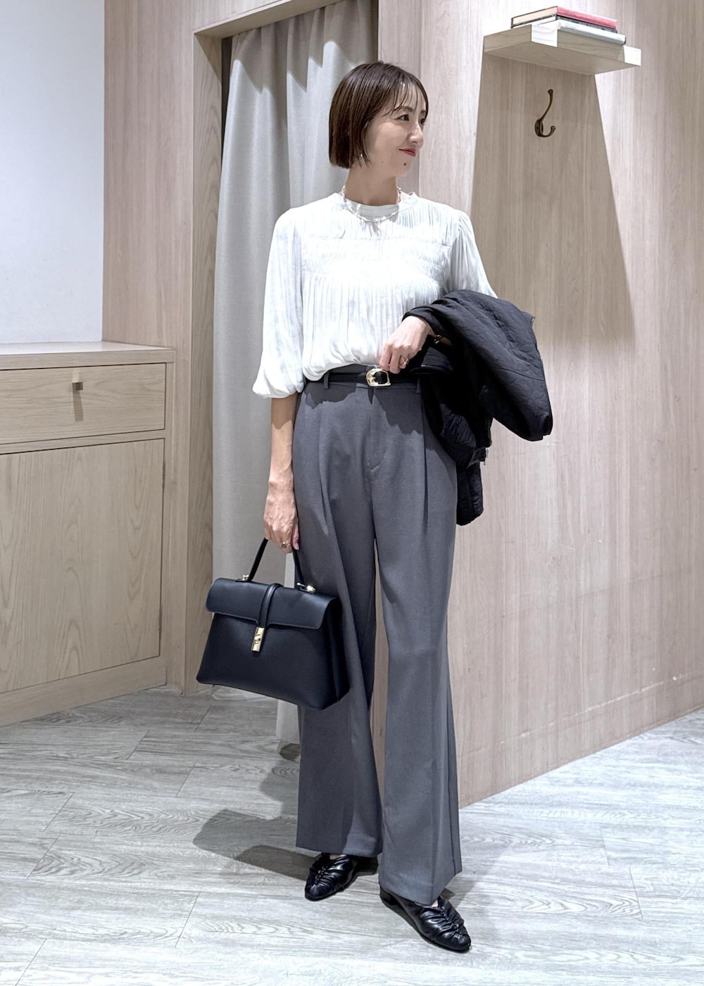 ブラック系のハンドバッグ、グレー系のスラックス、ホワイト系のシャツ/ブラウスを着用したレディースの秋コーディネートの2枚目の写真