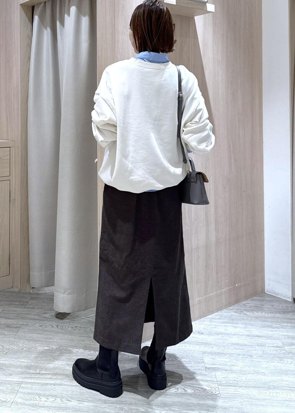 グレー系のショルダーバッグ、ブラック系のブーツ、ブラウン系のスカートを着用したレディースの秋コーディネートの2枚目の写真