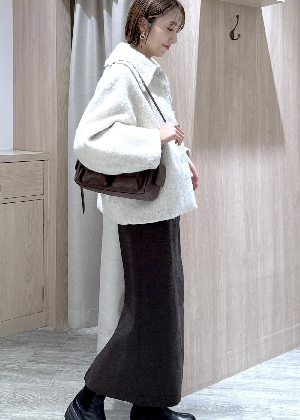 ブラウン系のショルダーバッグ、ブラック系のブーツ、ホワイト系のブルゾンを着用したレディースの秋コーディネートの3枚目の写真