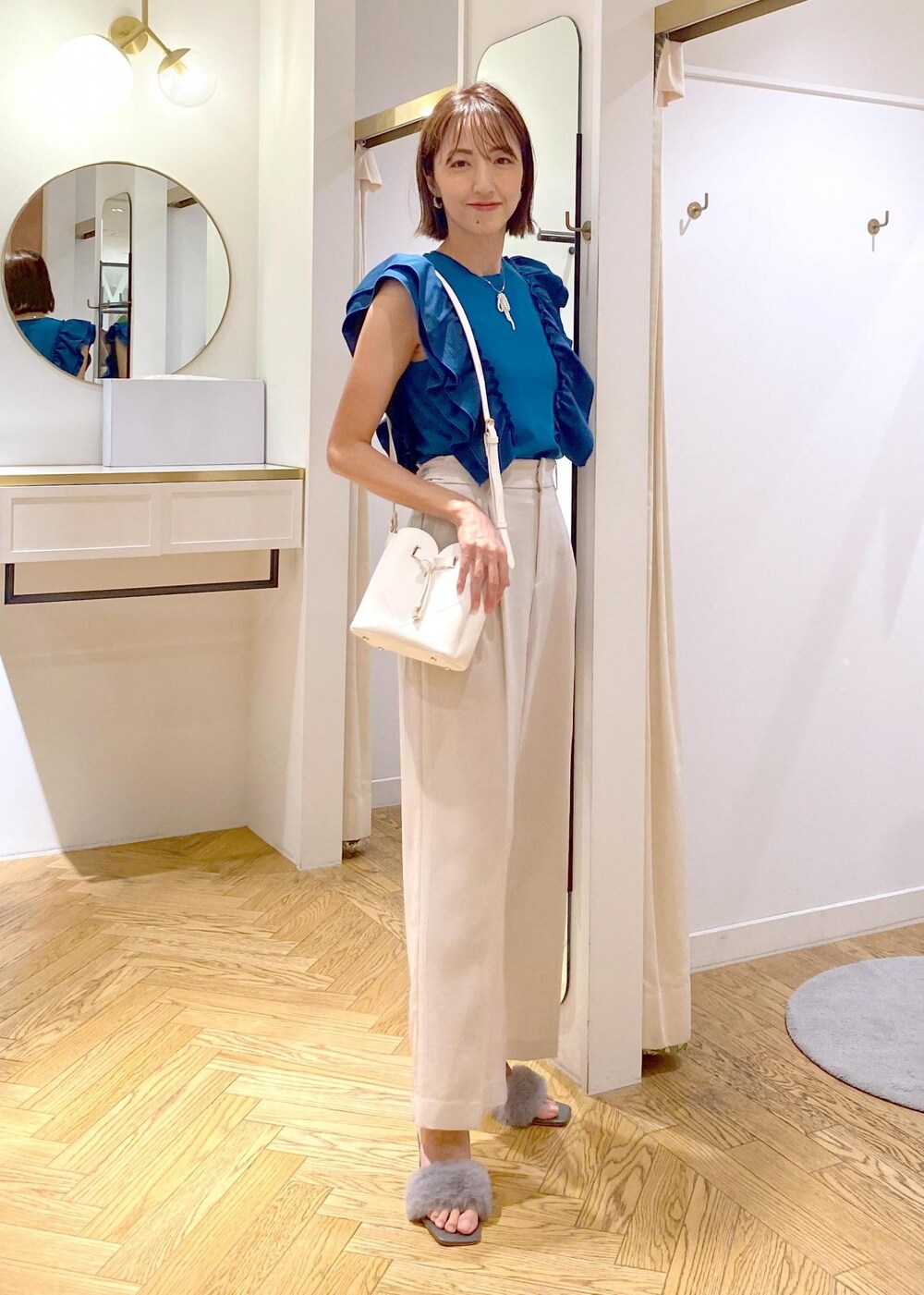 ホワイト系のスラックス、ホワイト系のショルダーバッグ、グレー系のドレスシューズを着用したレディースの夏コーディネートの2枚目の写真