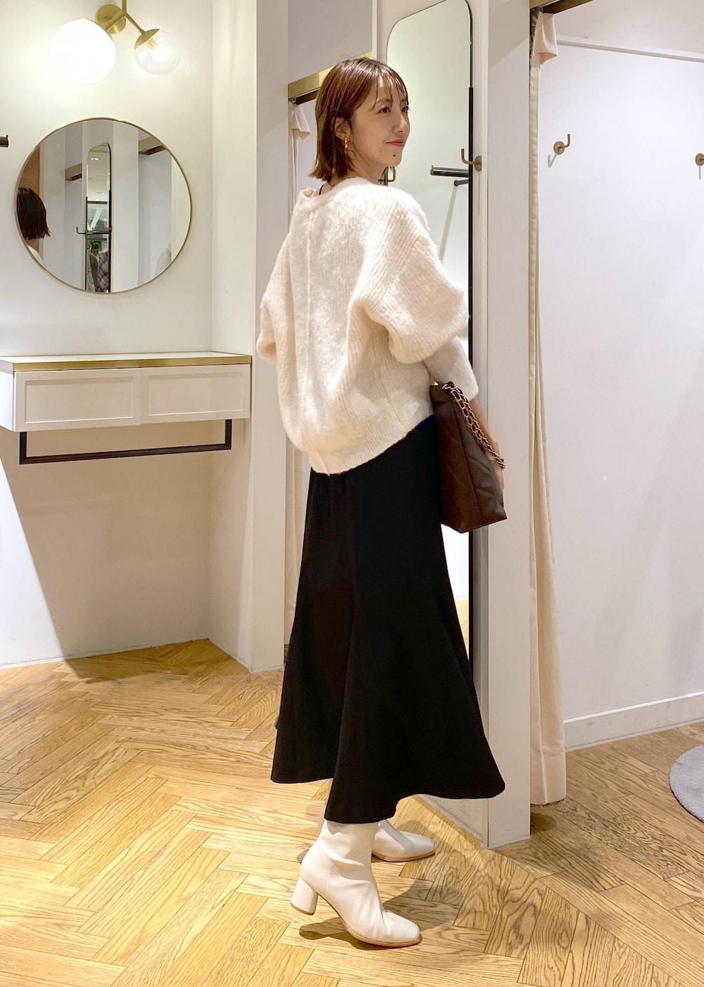 ホワイト系のブーツ、ブラック系のスカート、ブラウン系のショルダーバッグを着用したレディースの秋コーディネートの2枚目の写真