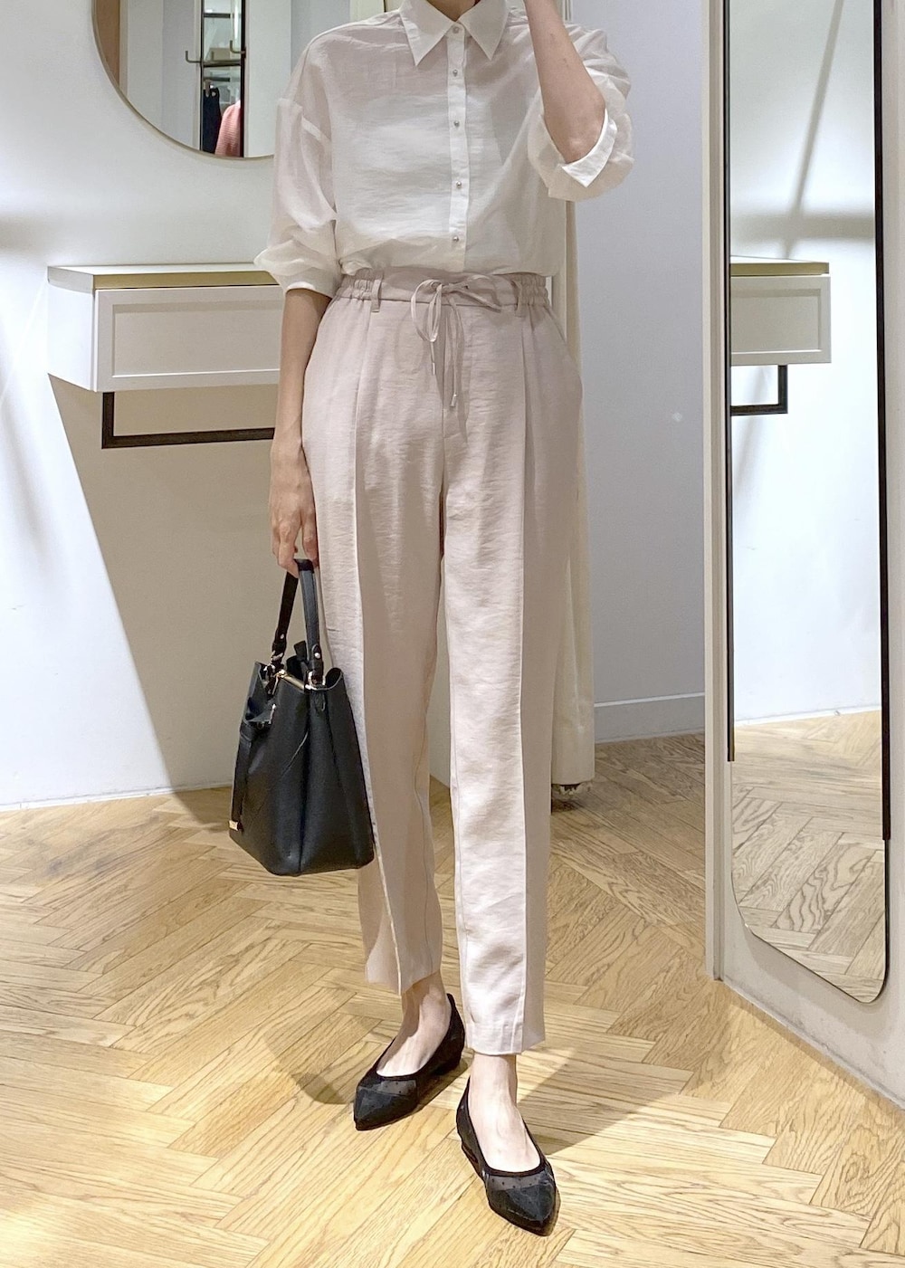 ブラック系のパンプス、ブラック系のハンドバッグ、ホワイト系のスラックスを着用したレディースの夏コーディネートの4枚目の写真