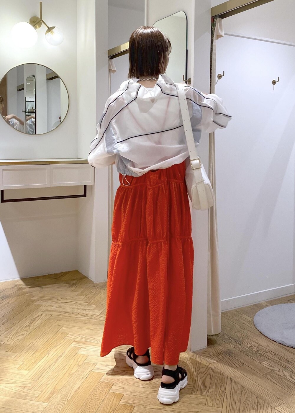 ホワイト系のショルダーバッグ、ブラック系のサンダル、オレンジ系のジャンパースカートを着用したレディースの春コーディネートの3枚目の写真