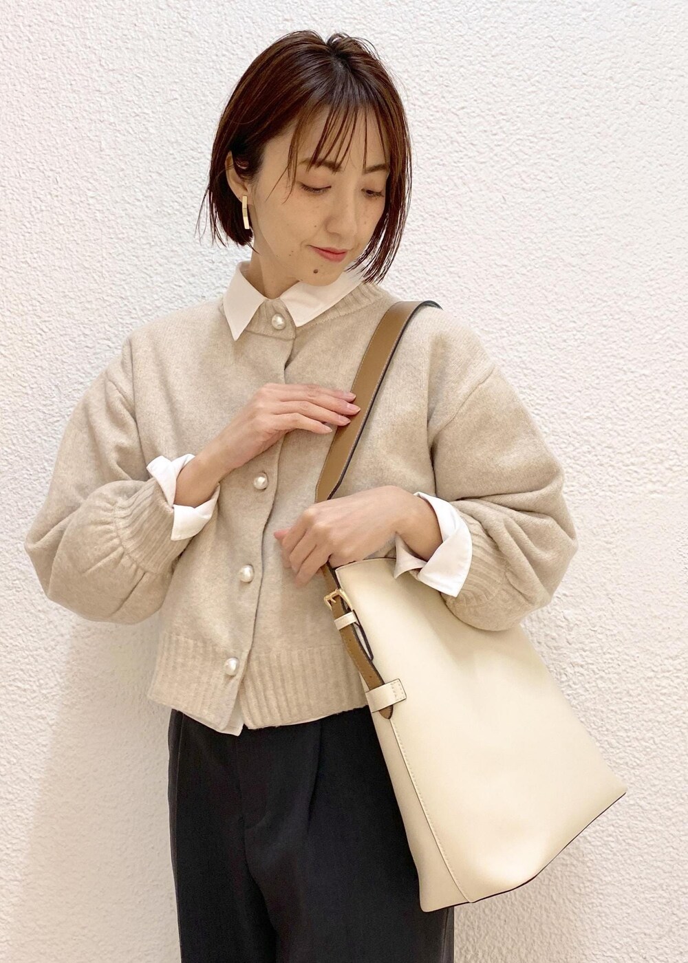 ベージュ系のカーディガン/ボレロ、グレー系のスラックス、ホワイト系のショルダーバッグを着用したレディースの冬コーディネートの4枚目の写真