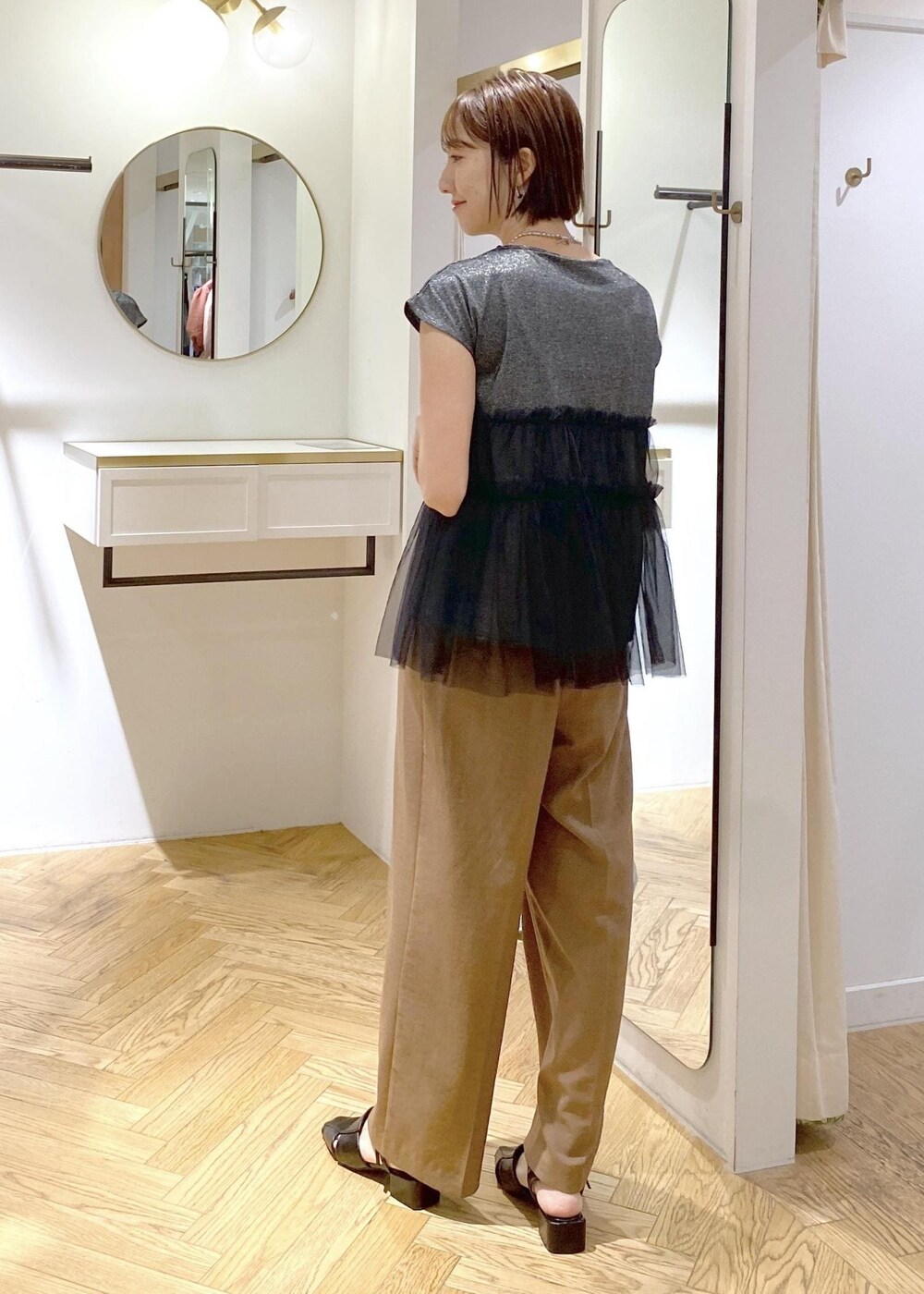 シルバー系のハンドバッグ、ブラック系のサンダル、ブラウン系のスラックスを着用したレディースの夏コーディネートの3枚目の写真