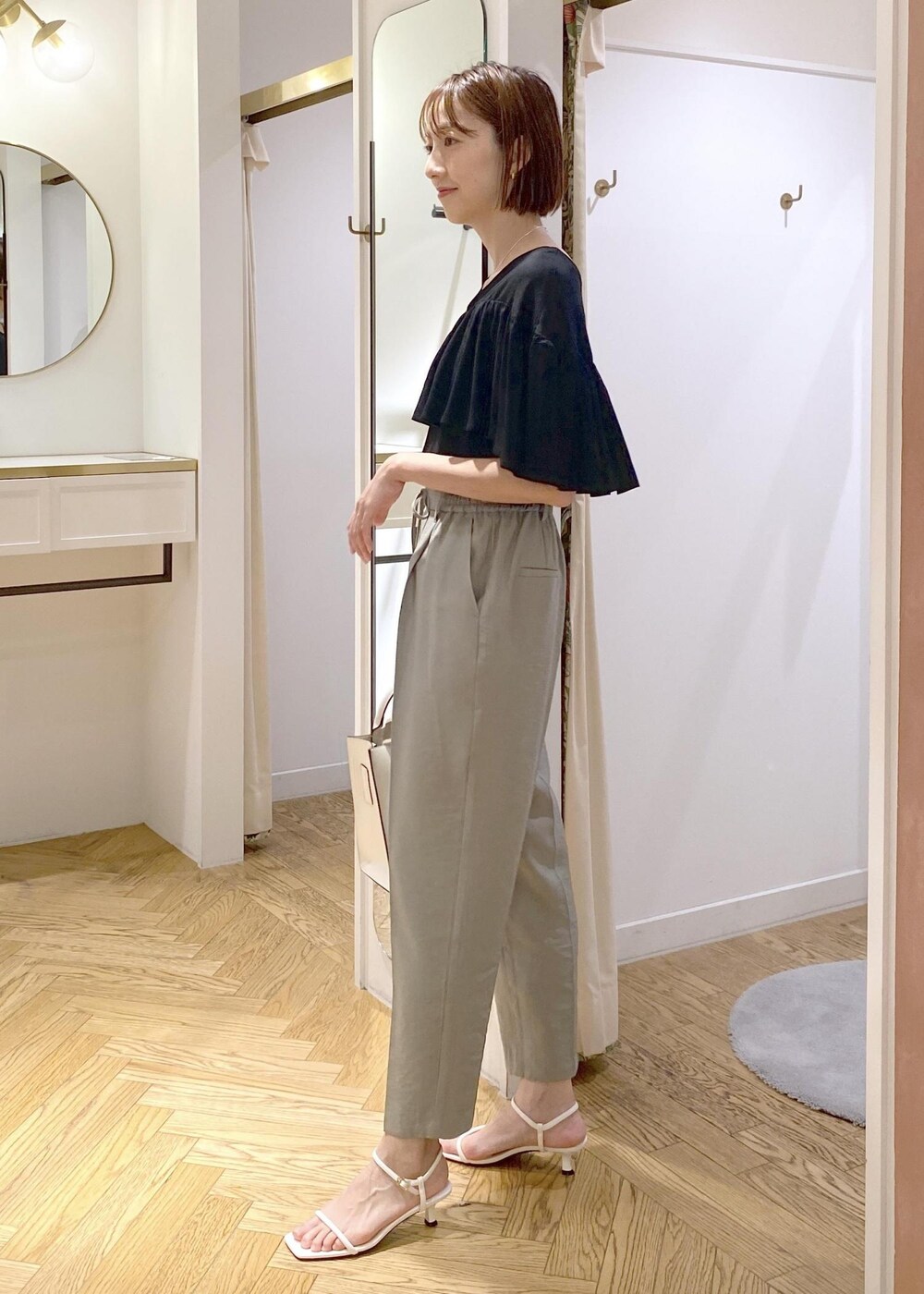 グリーン系のスラックス、ホワイト系のサンダル、ホワイト系のハンドバッグを着用したレディースの夏コーディネートの2枚目の写真