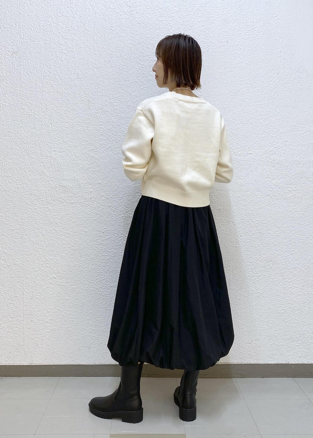 ブラック系のブーツ、ブラック系のスカート、グリーン系のショルダーバッグを着用したレディースの冬コーディネートの2枚目の写真