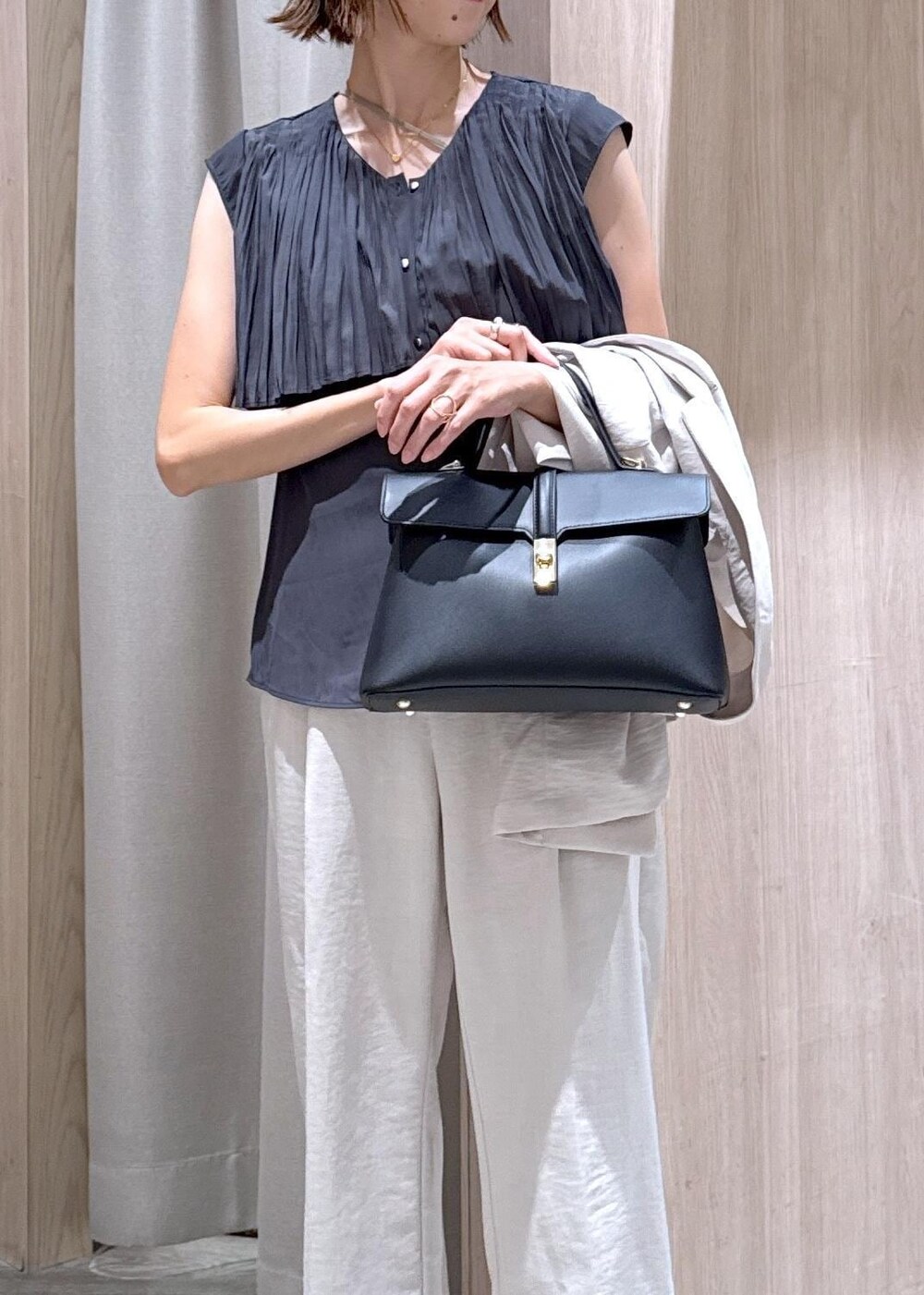 ブラック系のハンドバッグ、ブラック系のパンプス、ホワイト系のスラックスを着用したレディースの夏コーディネートの7枚目の写真