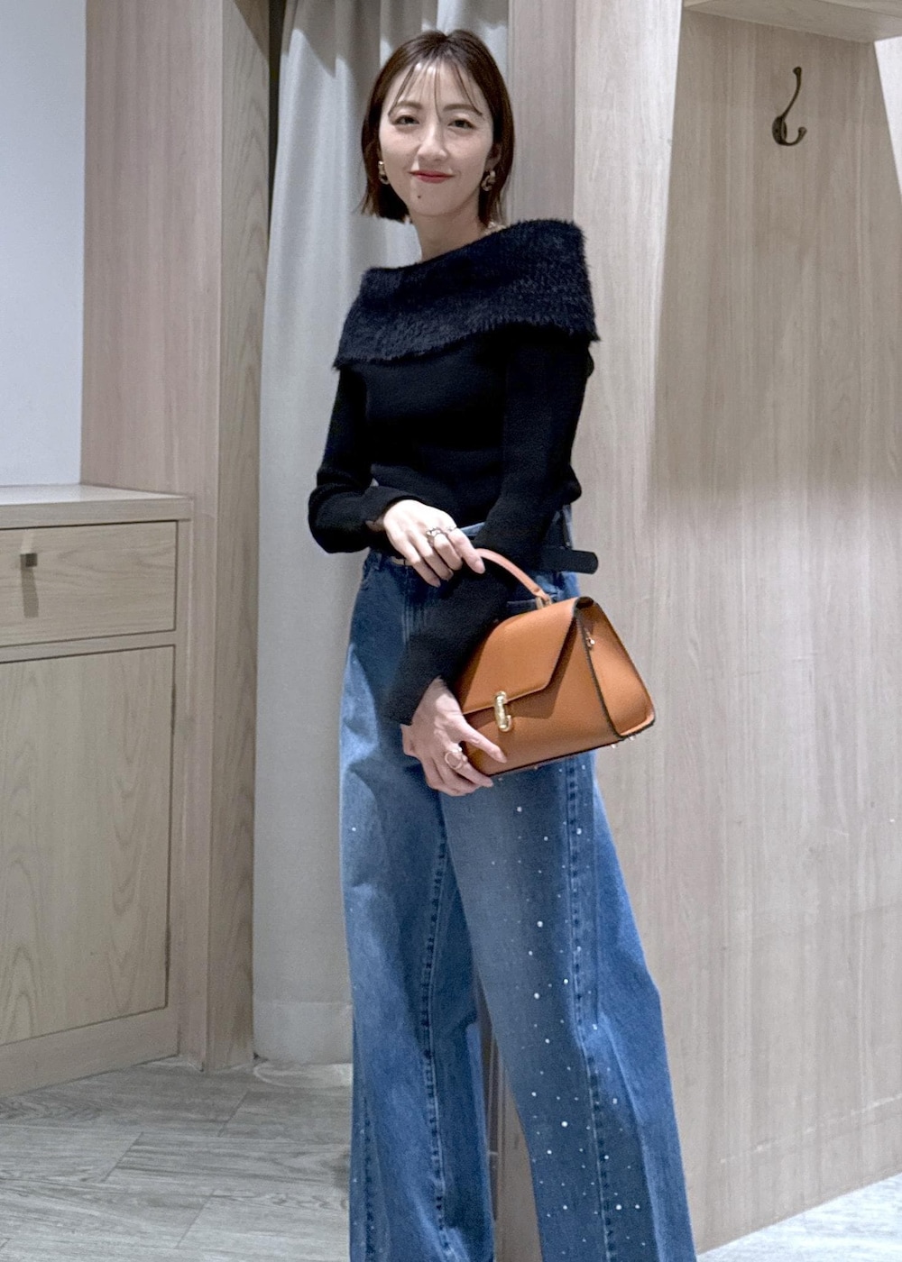 ブルー系のデニムパンツ、イエロー系のハンドバッグ、ブラック系のニット/セーターを着用したレディースの冬コーディネートの2枚目の写真