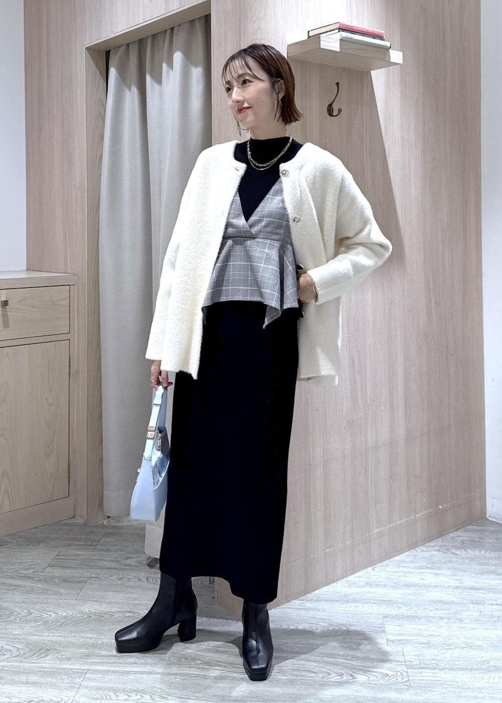 ブルー系のハンドバッグ、ホワイト系のノーカラージャケット、ブラック系のブーツを着用したレディースの秋コーディネートの2枚目の写真