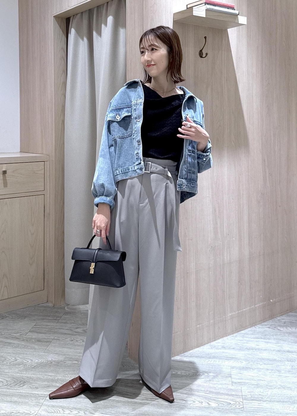 ブラック系のショルダーバッグ、ブルー系のデニムジャケット、グレー系のスラックスを着用したレディースの春コーディネートの2枚目の写真