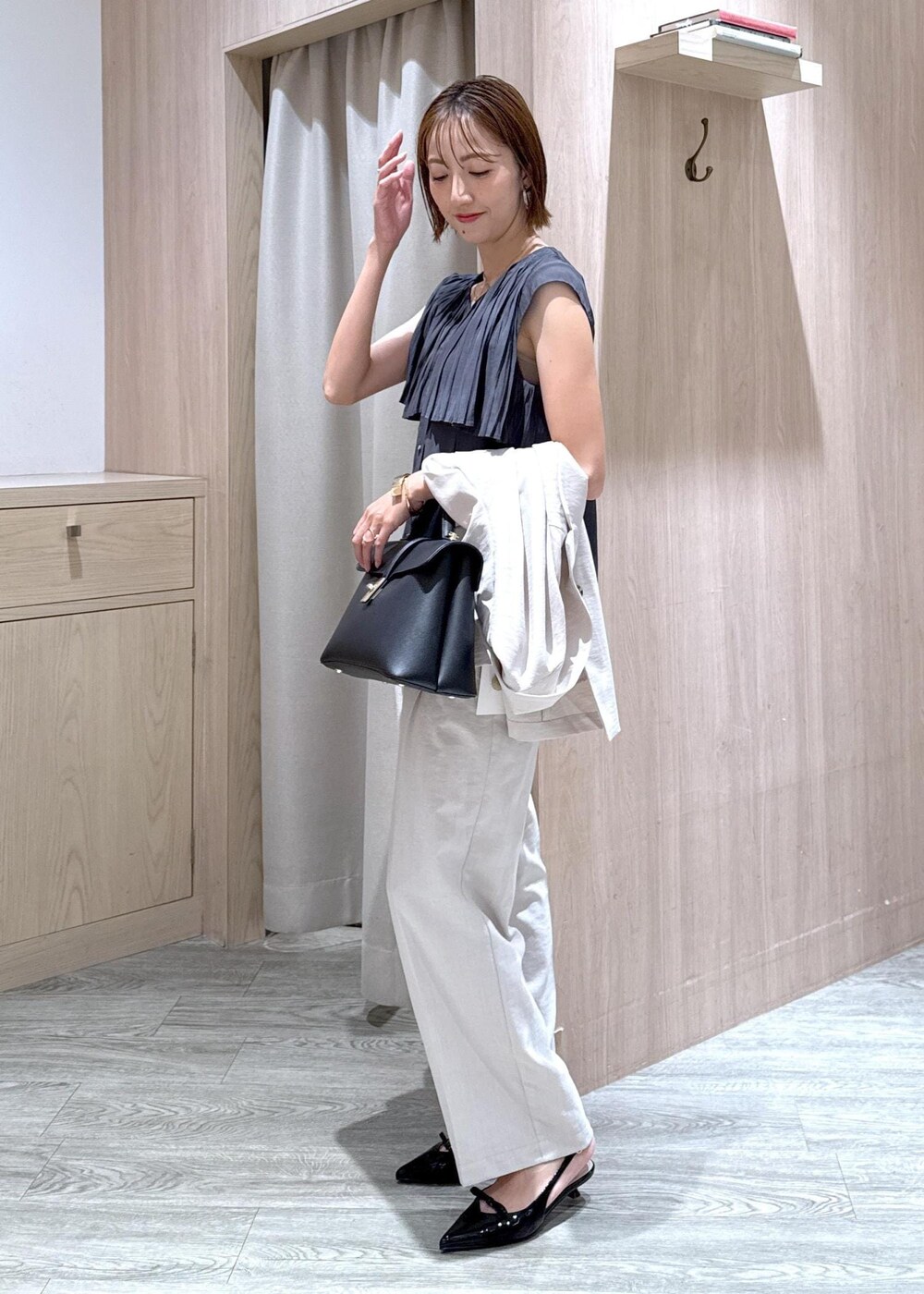 ブラック系のハンドバッグ、ブラック系のパンプス、ホワイト系のスラックスを着用したレディースの夏コーディネートの3枚目の写真