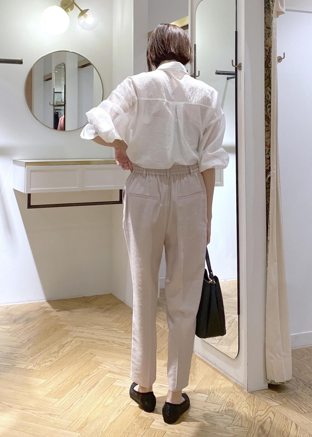 ブラック系のパンプス、ブラック系のハンドバッグ、ホワイト系のスラックスを着用したレディースの夏コーディネートの3枚目の写真