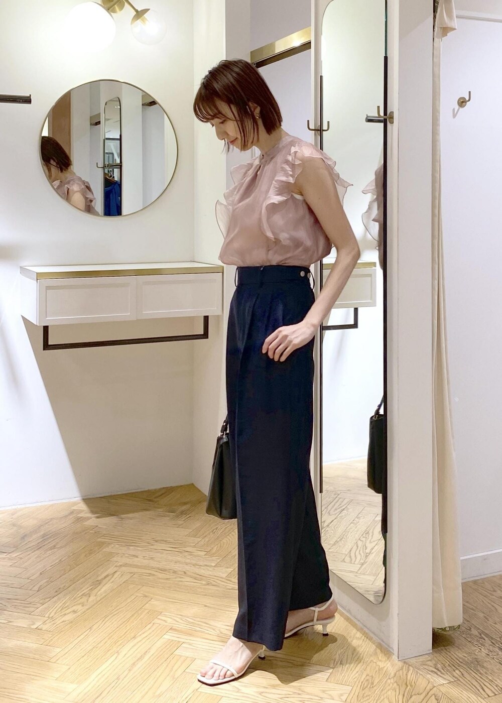 ブルー系のスラックス、ブラック系のハンドバッグ、ホワイト系のキャミソールを着用したレディースの春コーディネートの2枚目の写真