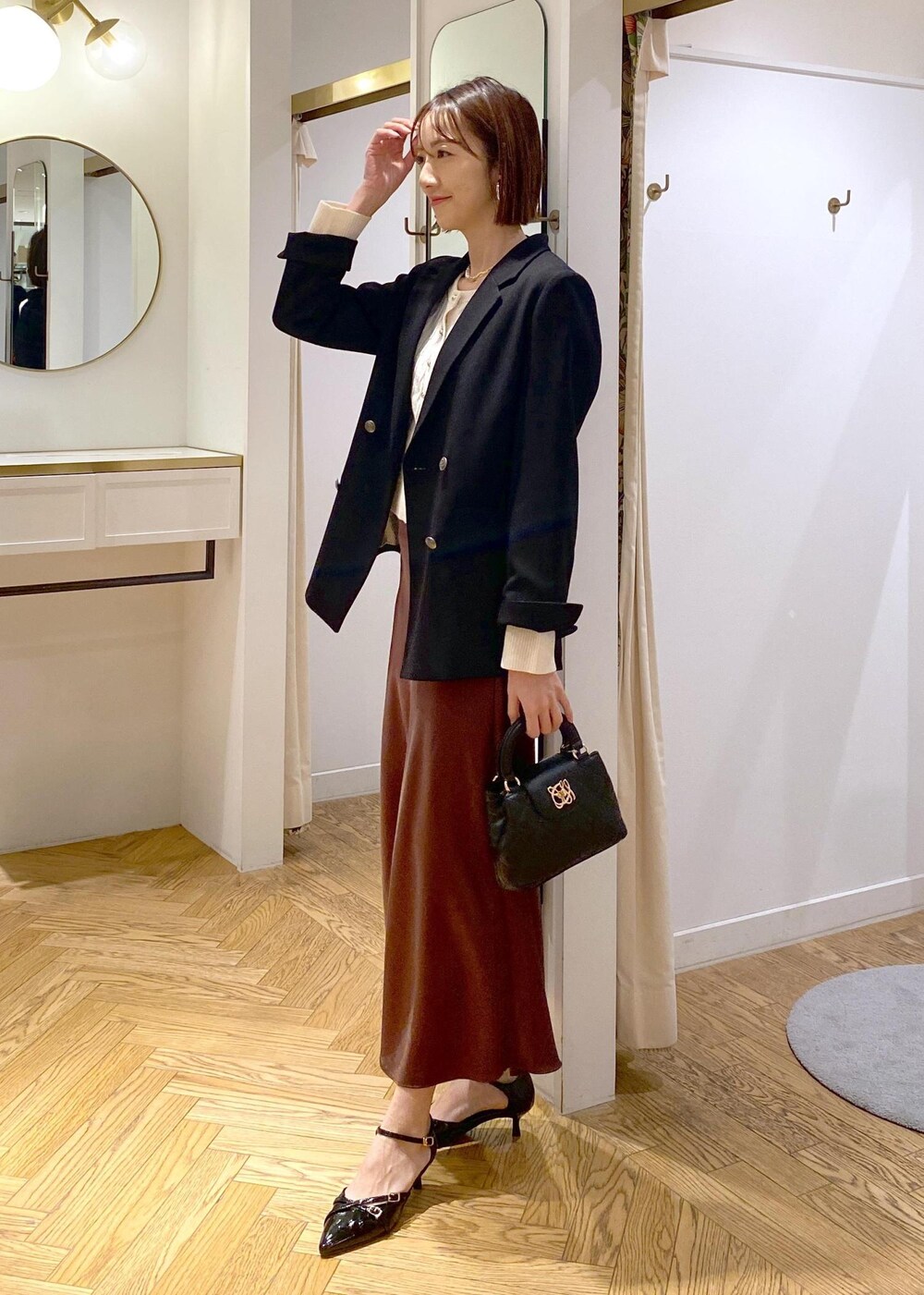ブラック系のテーラードジャケット、ブラック系のパンプス、ブラウン系のスカートを着用したレディースの冬コーディネートの2枚目の写真