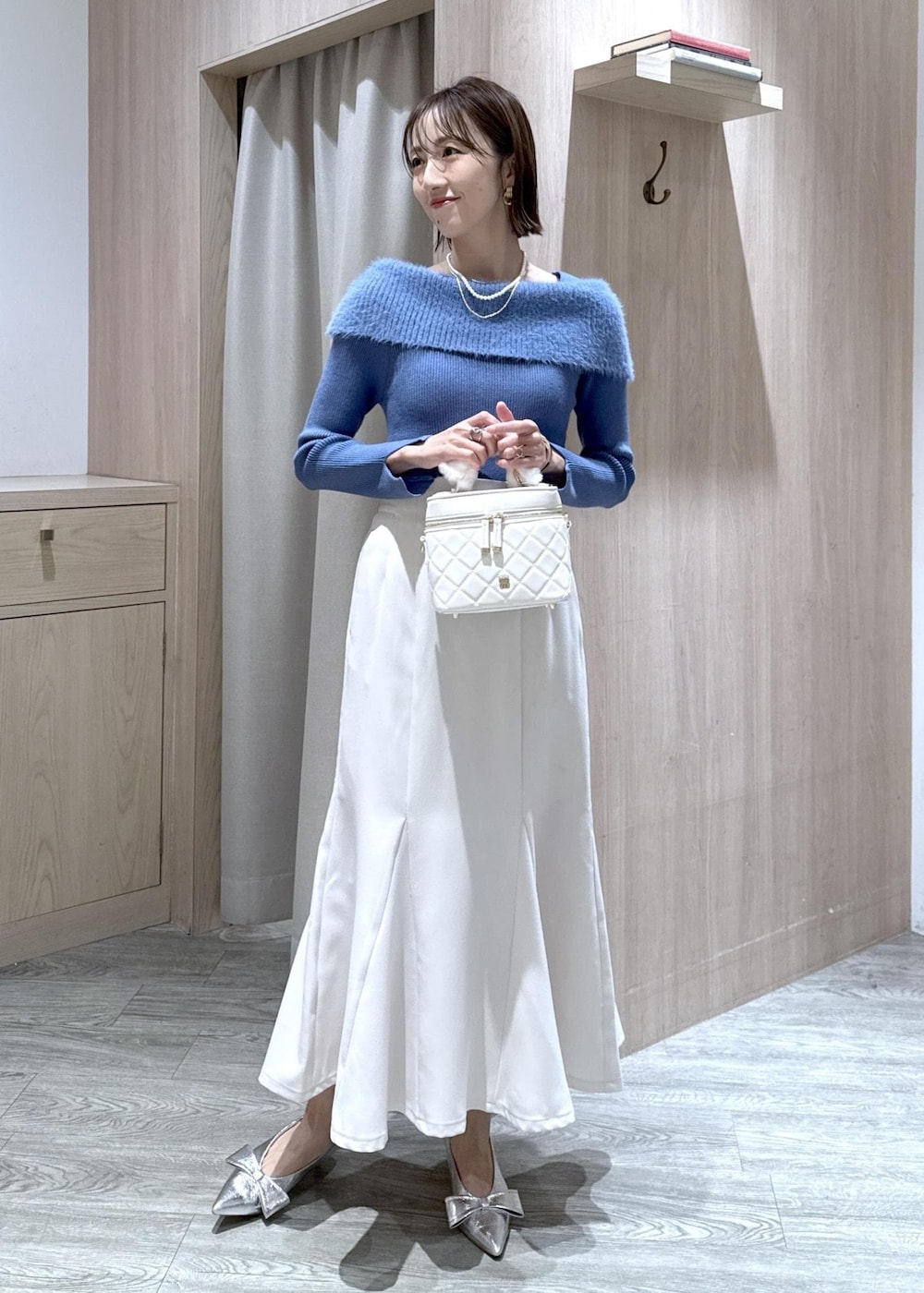 シルバー系のパンプス、ホワイト系のハンドバッグ、ブルー系のニット/セーターを着用したレディースの秋コーディネートの4枚目の写真