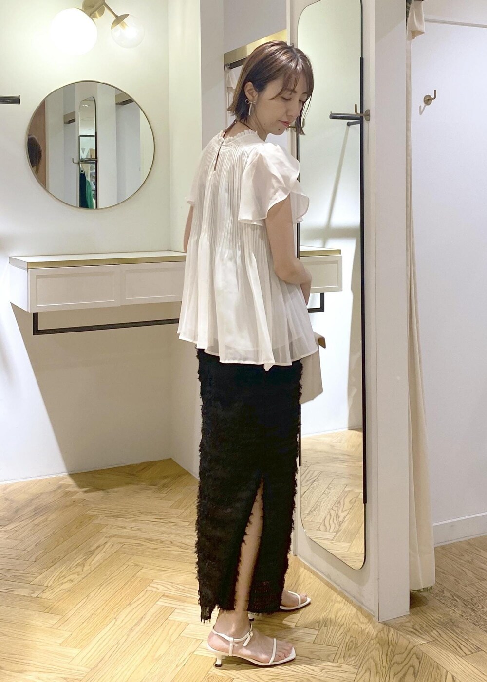 ホワイト系のハンドバッグ、ホワイト系のサンダル、ブラック系のスカートを着用したレディースの春コーディネートの2枚目の写真